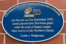 Blue metal plaque on brick wall, with text on about Leeds playing their first home game against Brighouse in 1895