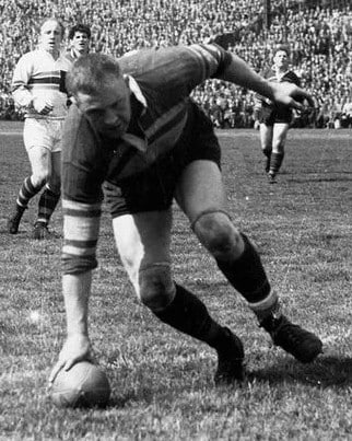 black and white photo of Jack Fairbanks touching the ruby ball down mid-play on the field