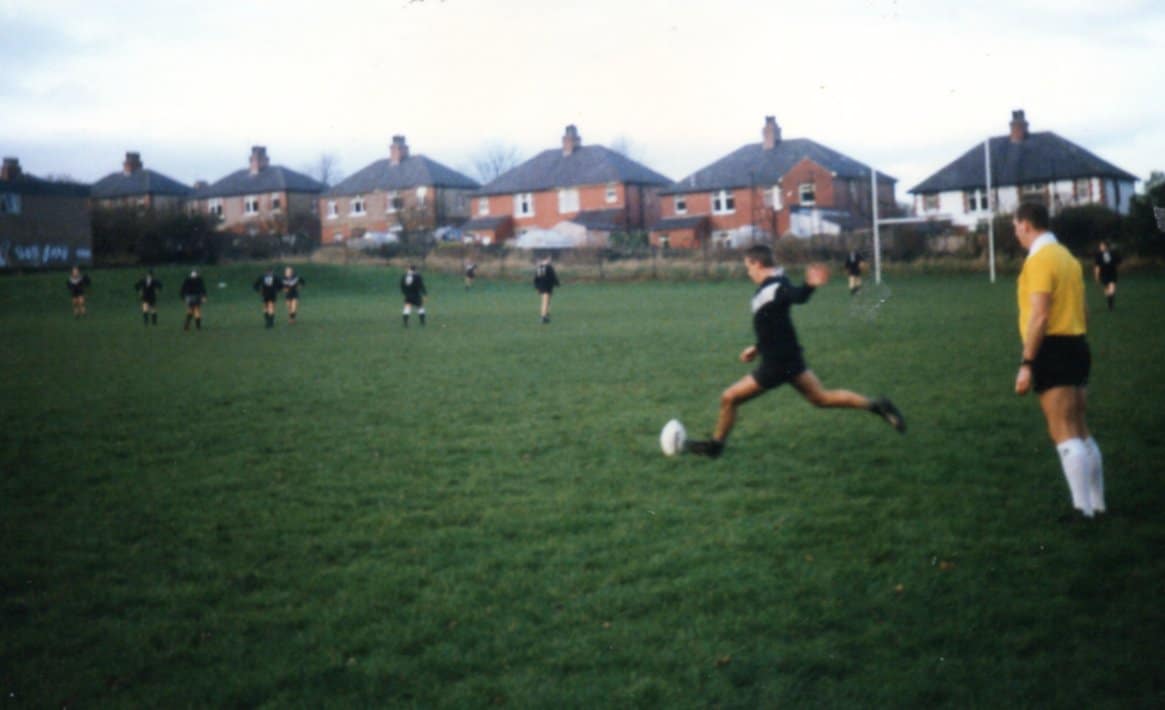 old colour photo of a match, one person in a dark kit is about to kick the ball