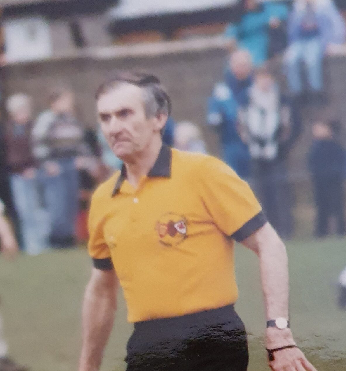 colour photo of a referee mid-match, wearing a yellow tshirt
