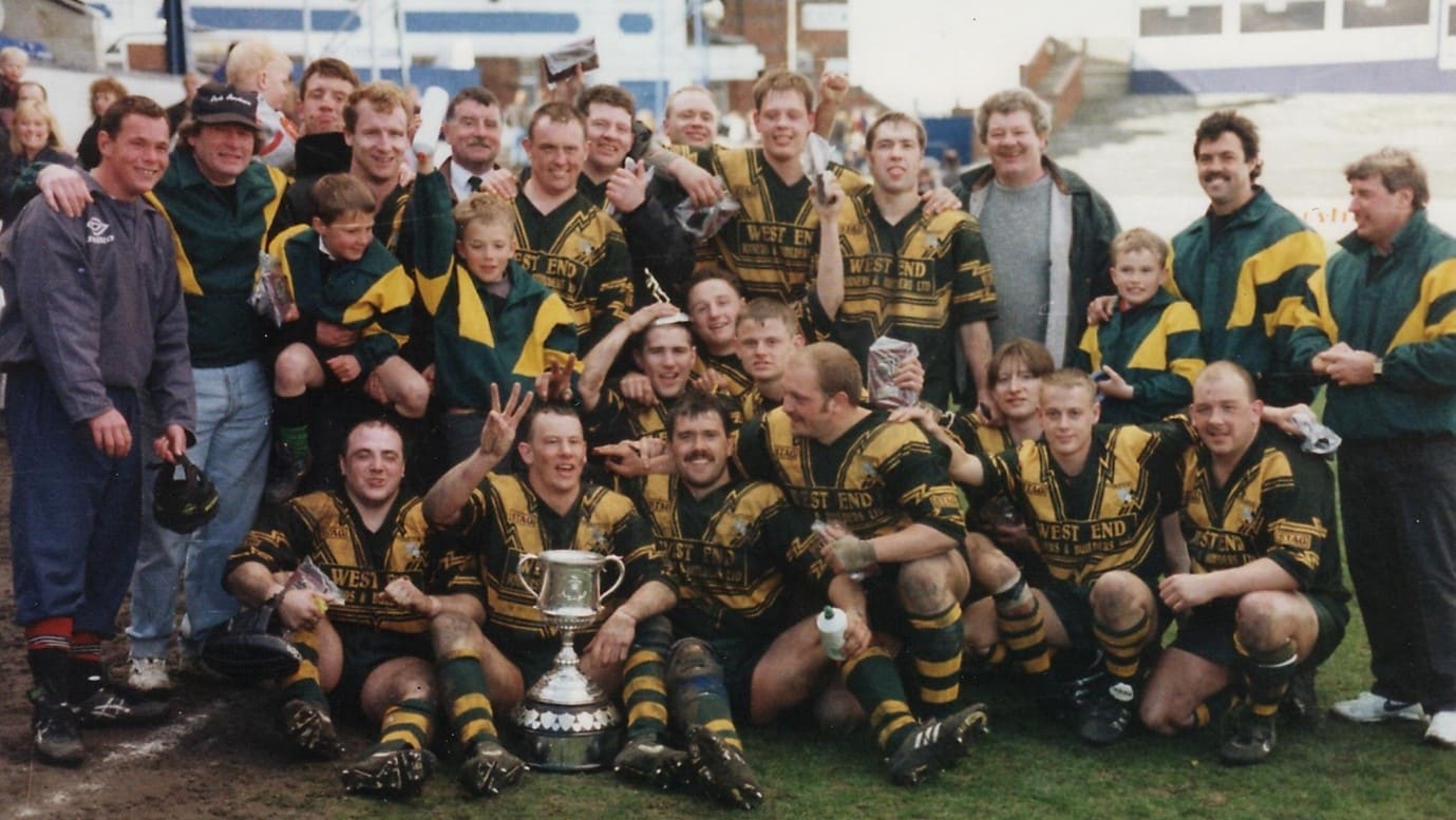 colour photo of team members, wearing their kits, smiling and holding trophies