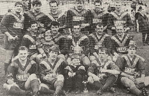 black and white photo of three rows of team players, wearing their kits and holding trophies