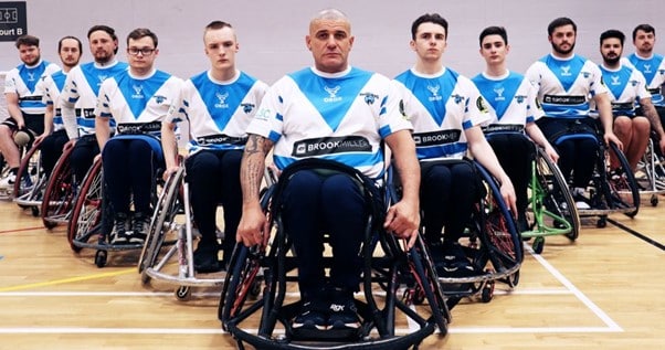 colour photo of wheelchair rugby league team in their kits in a v-formation on the court