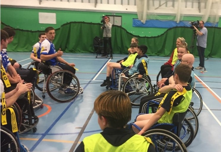 colour mid-match photo of a wheelchair rugby league match on the court, one team are wearing luminous yellow bibs