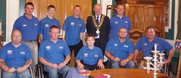 Wheelchair team wearing mid blue polo shirts, smiling for photo with Halifax mayor
