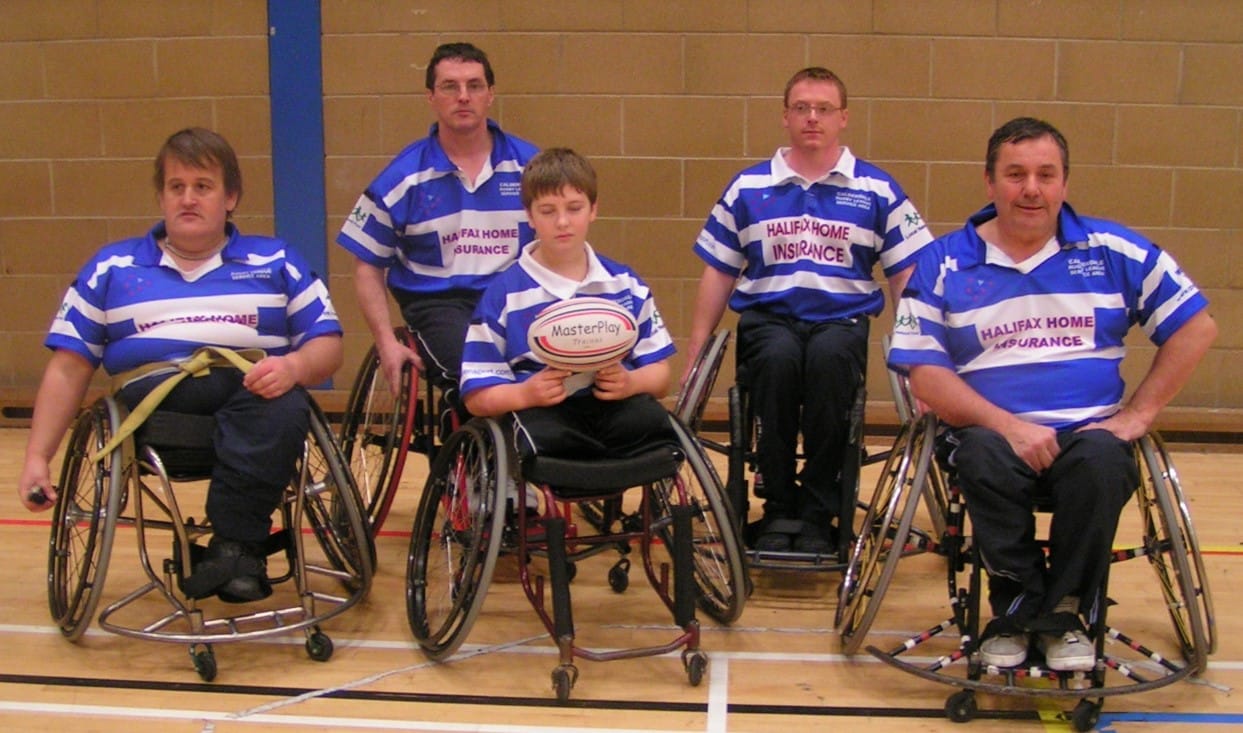 five members of the wheelchair team looking forward for the photo, wearing their kits, the person in the middle is holding a rugby ball
