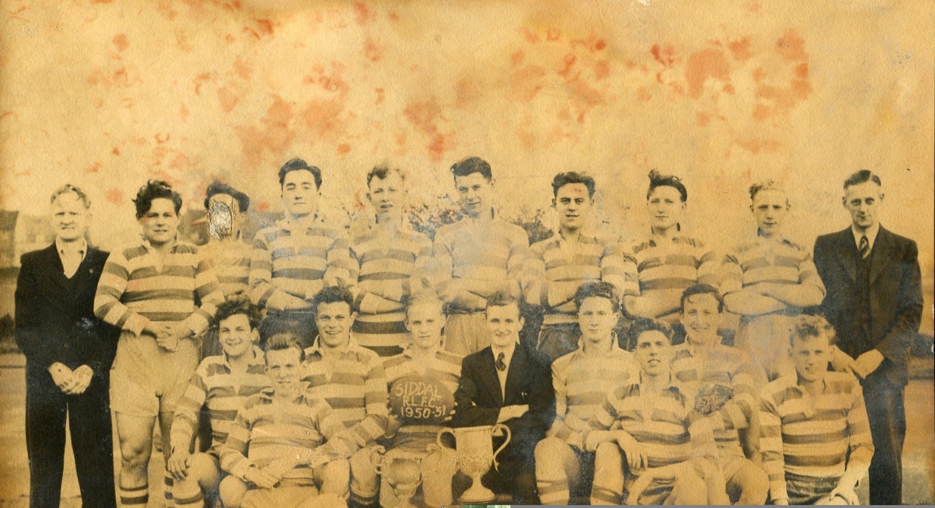 sepia photo of Siddal team in 1951, platers are in two rows, wearing stripey kits and there is a person either side wearing a dark suit, and one sat in the middle holding the trophy cup
