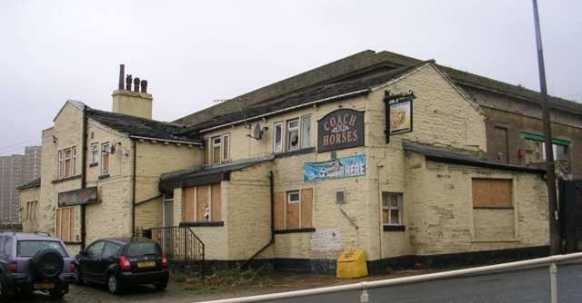colour photo of the exterior of The Coach and Horses in Boothtown's building- which is painted with a light yellow and has boarded up windows