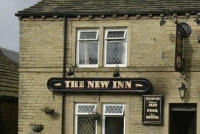colour photo of the part of the exterior of The New Inn building, which has sandstone coloured brick and a sign 