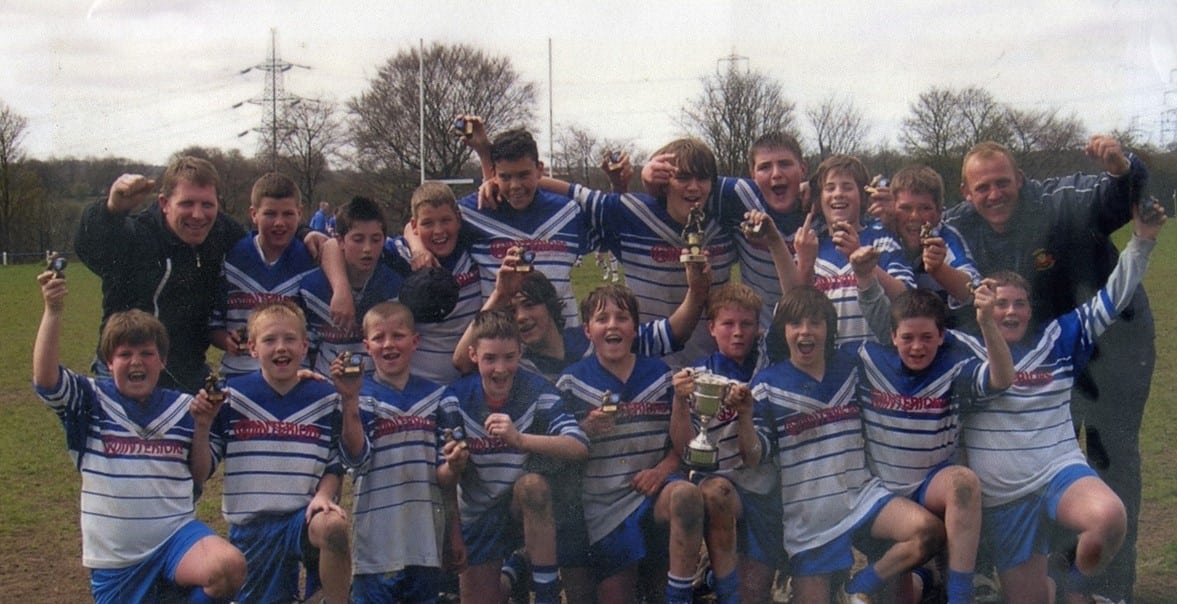 colour photo of juniors team in their kits, celebrating on the pitch
