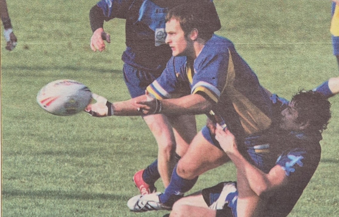 colour newspaper action photo of a player throwing the ball whilst being tackled on the pitch
