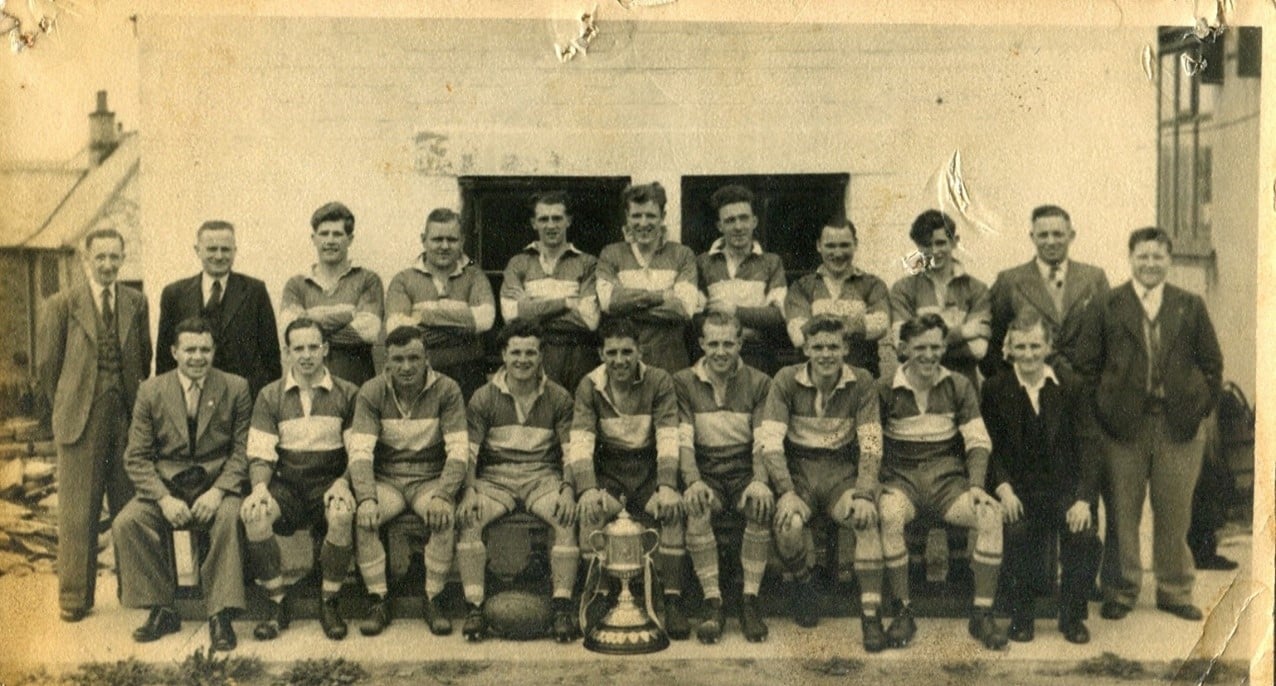 old black and white photo of the Siddal team, in two rows outside a building, wearing their kits, a few people are standing and sitting either side wearing suits