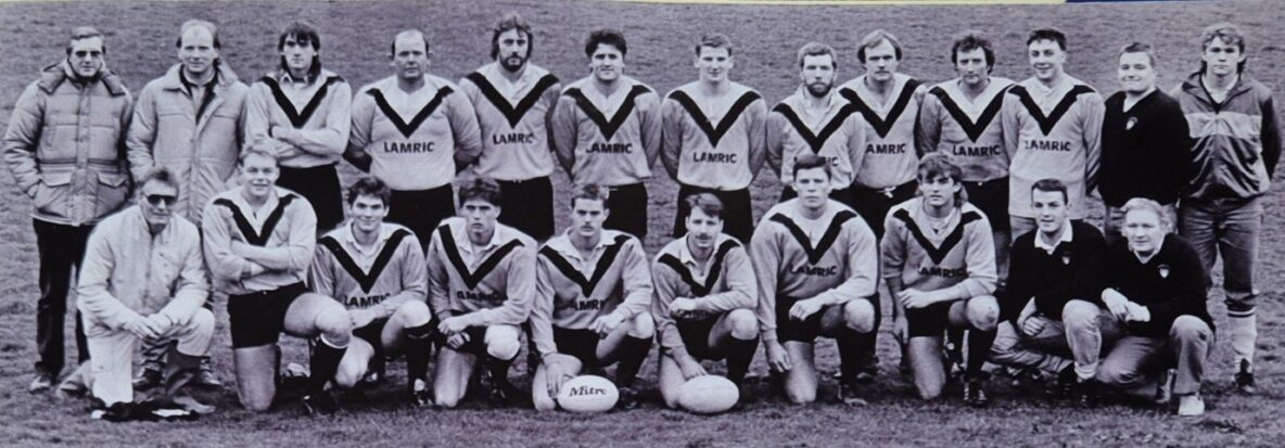 black and white photo of team in two rows with two rugby balls at the front in the middle