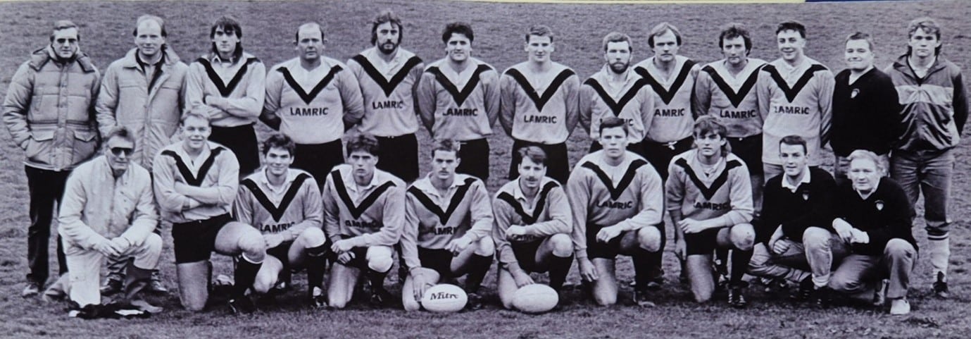 black and white photo of team in two rows with two rugby balls at the front in the middle 