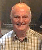 colour headshot photo of Barry Dyson who is smiling, has light grey hair and is wearing a check shirt with the top button undone 
