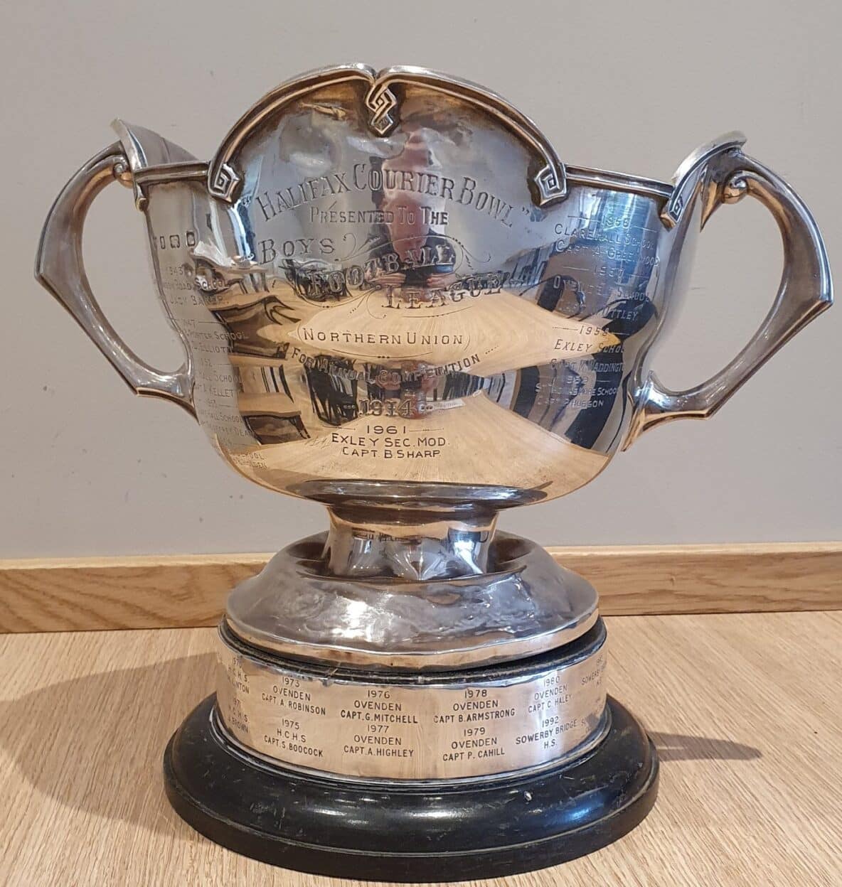 Colour photo of the silver Halifax Couriers Cup trophy on a light wooden surface. The cup is shiny and has two handles on the sides and a dark, round wooden base