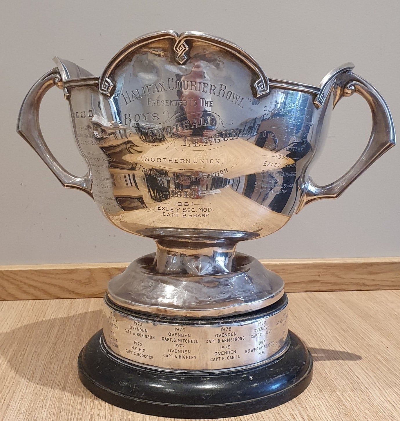 Colour photo of the silver Halifax Couriers Cup trophy on a light wooden surface. The cup is shiny and has two handles on the sides and a dark, round wooden base