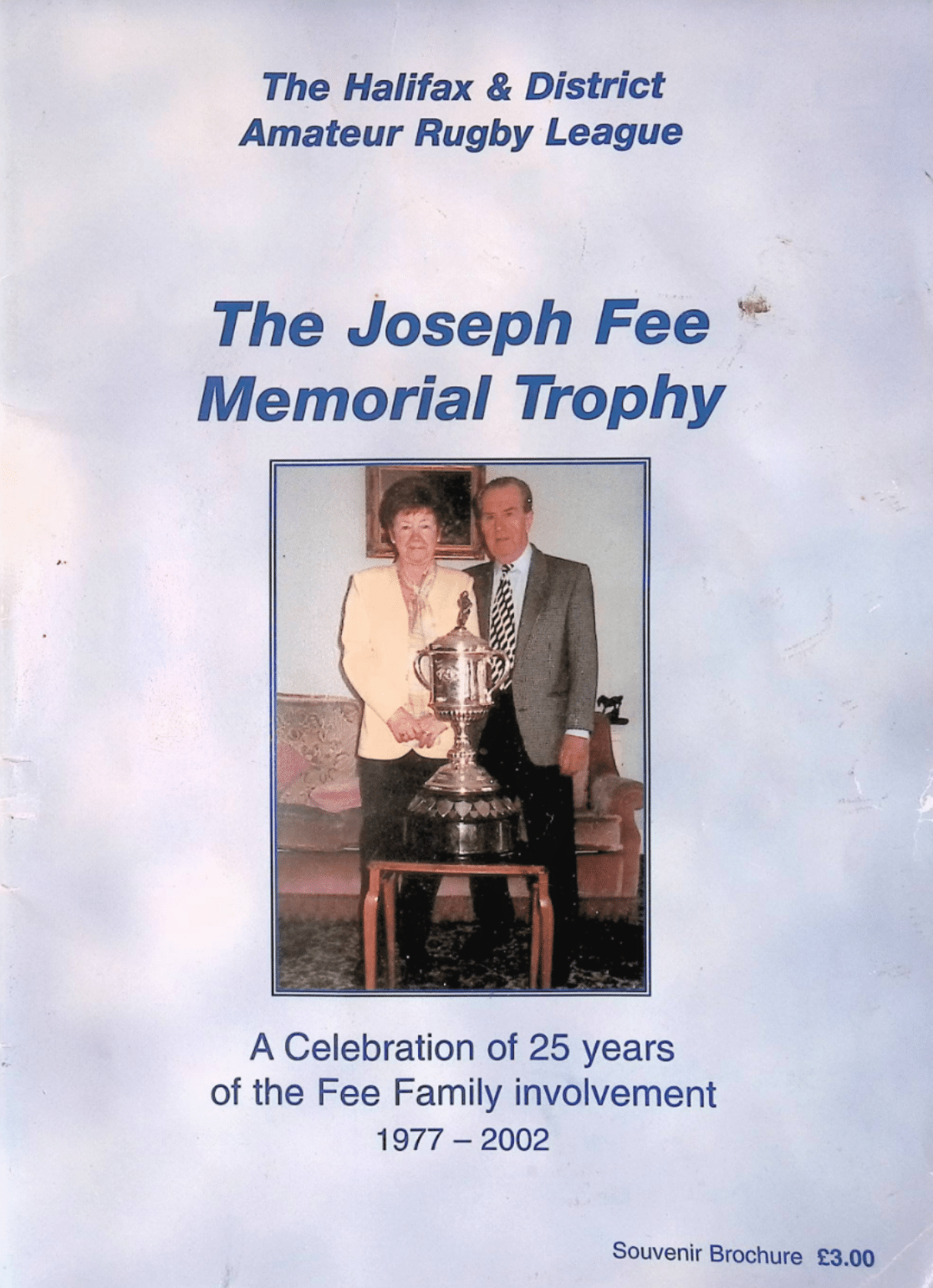 Colour scan of Joseph Fee Memorial Trophy Celebration Programme cover- which has a light blue background, a photo of Fee and a person beside them, standing in front of a trophy